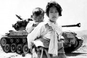 A weary Korean girl, carrying her brother on her back, walks past an M-26 tank in Haengju, Korea. June 9, 1951.